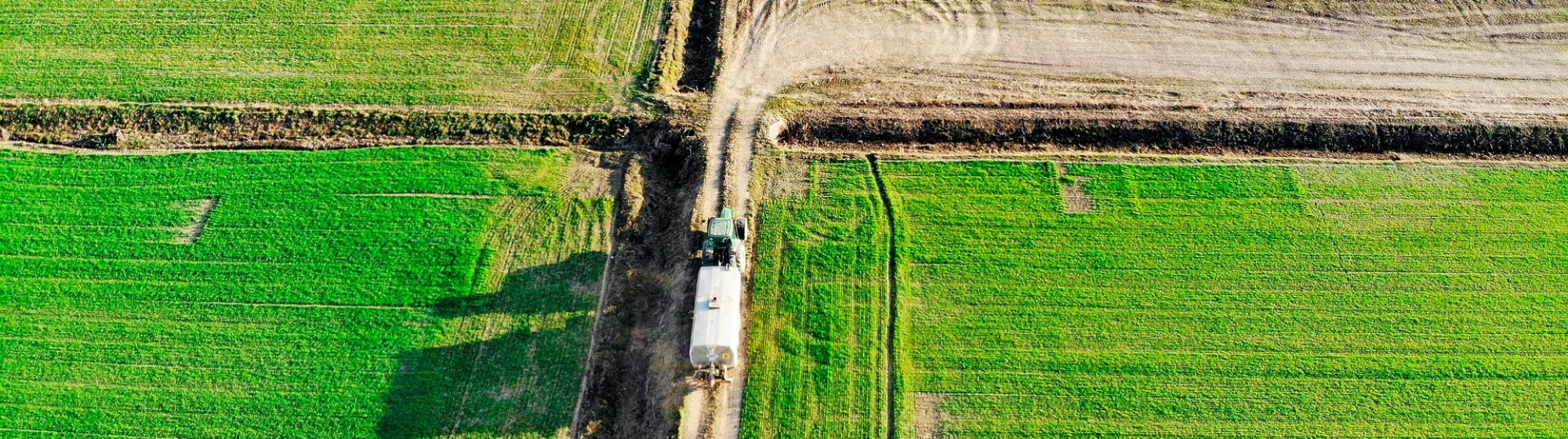 Luchtfoto van groene landbouwpercelen met een tractor die op een zandpad rijdt 