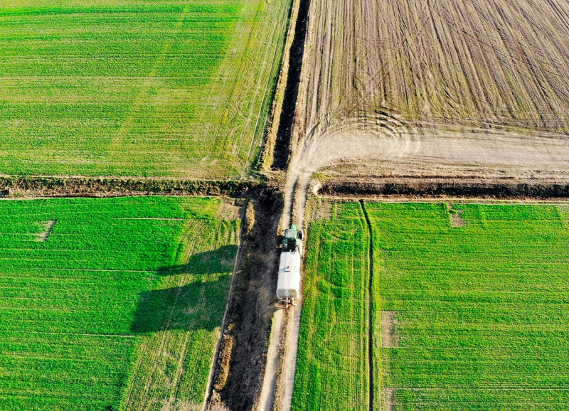 Luchtfoto van groene landbouwpercelen met een tractor die op een zandpad rijdt 