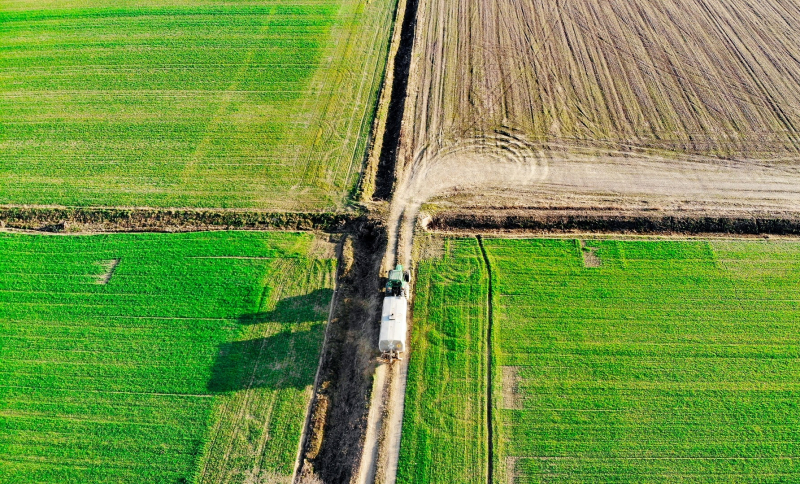 Luchtfoto van groene landbouwpercelen met een tractor die op een zandpad rijdt 