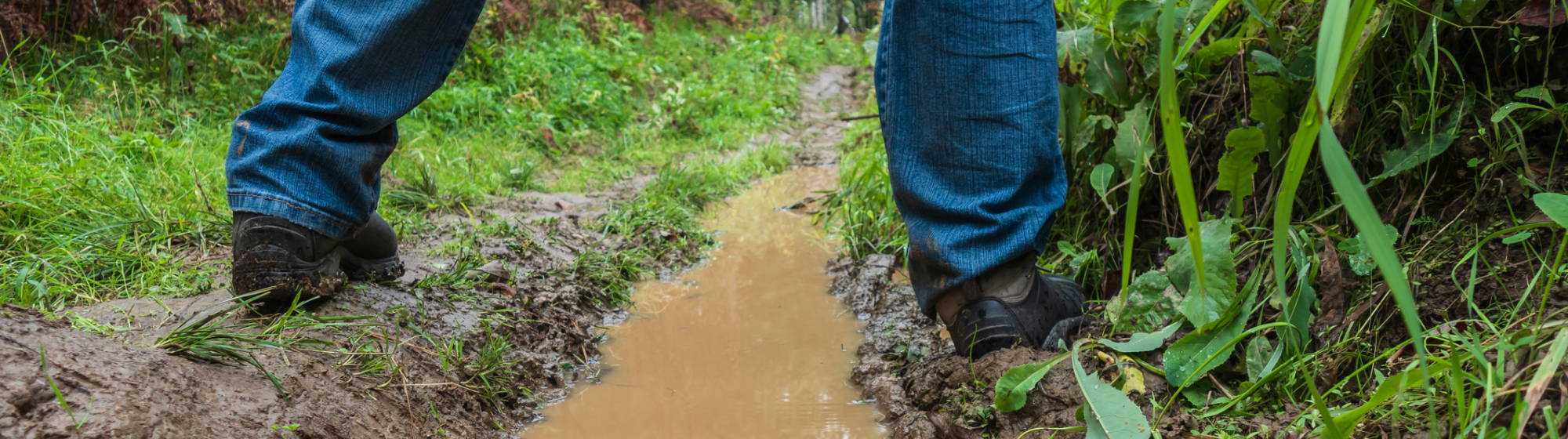 Twee benen op een modderig pad met waterplas in het buitengebied, illustratie van waterbeheer, bodemkwaliteit en klimaatadaptatie.