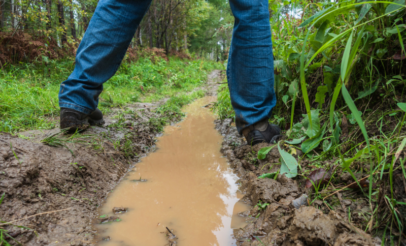 Twee benen op een modderig pad met waterplas in het buitengebied, illustratie van waterbeheer, bodemkwaliteit en klimaatadaptatie.