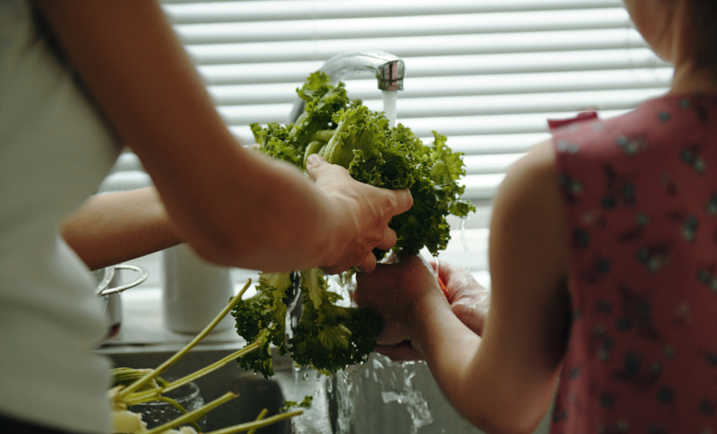 Twee personen wassen samen een krop groene sla onder stromend water.