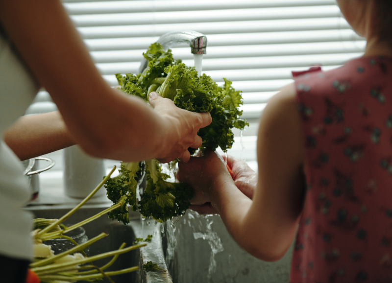 Twee personen wassen samen een krop groene sla onder stromend water.