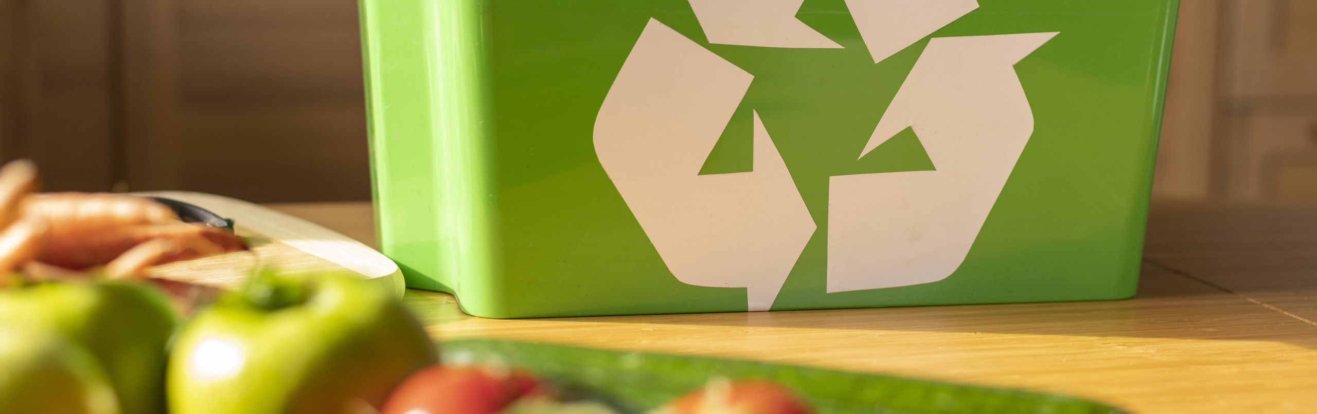 Foto van een groenrecylcebak met op de voorgrond appels, komkommers en tomaten 
