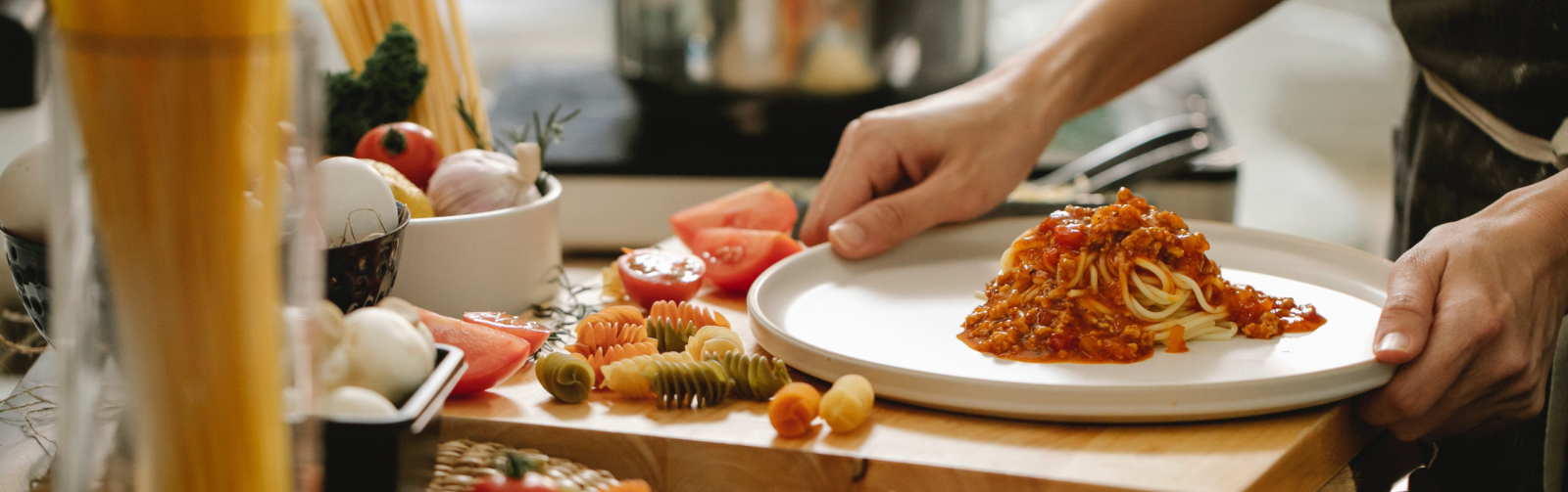 Foto van aanrecht met ingrediënten voor een spaghettimaaltijd en een persoon die pasta heeft opgeschept