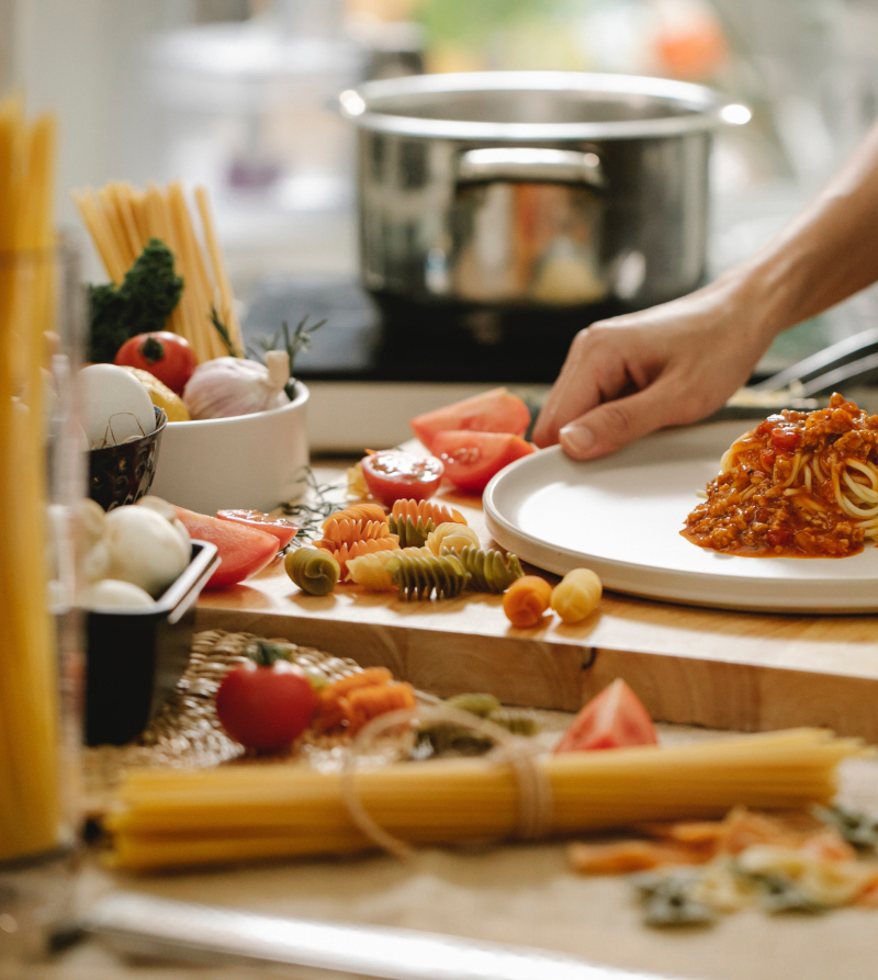 Foto van aanrecht met ingrediënten voor een spaghettimaaltijd en een persoon die pasta heeft opgeschept