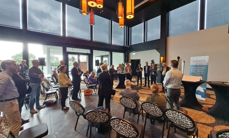 Deelnemers bestuurlijke Regioheidag staan pratend met elkaar in een zaal