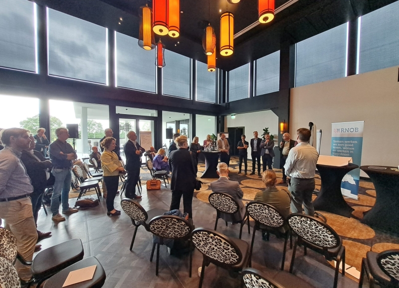 Deelnemers bestuurlijke Regioheidag staan pratend met elkaar in een zaal