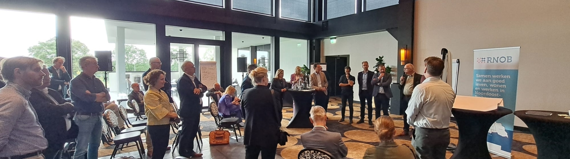 Deelnemers bestuurlijke Regioheidag staan pratend met elkaar in een zaal