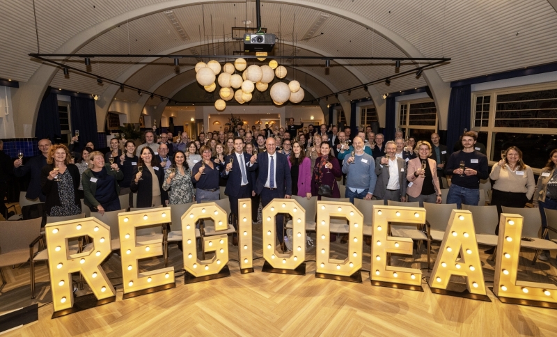 Groepsfoto van deelnemers aan het Regio Deal slotevent achter het woord Regio Deal in grote lichtgevende letters