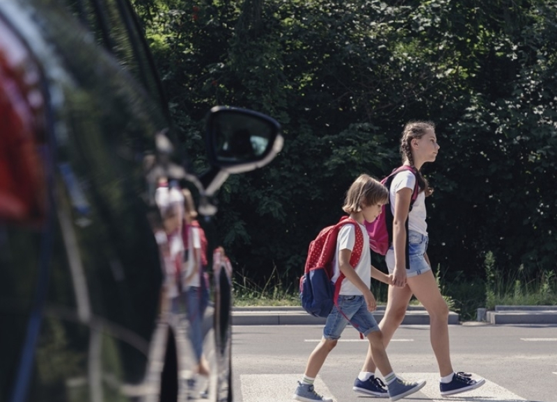 Kinderen steken over bij een zebrapad met een auto ervoor