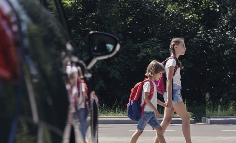 Kinderen steken over bij een zebrapad met een auto ervoor
