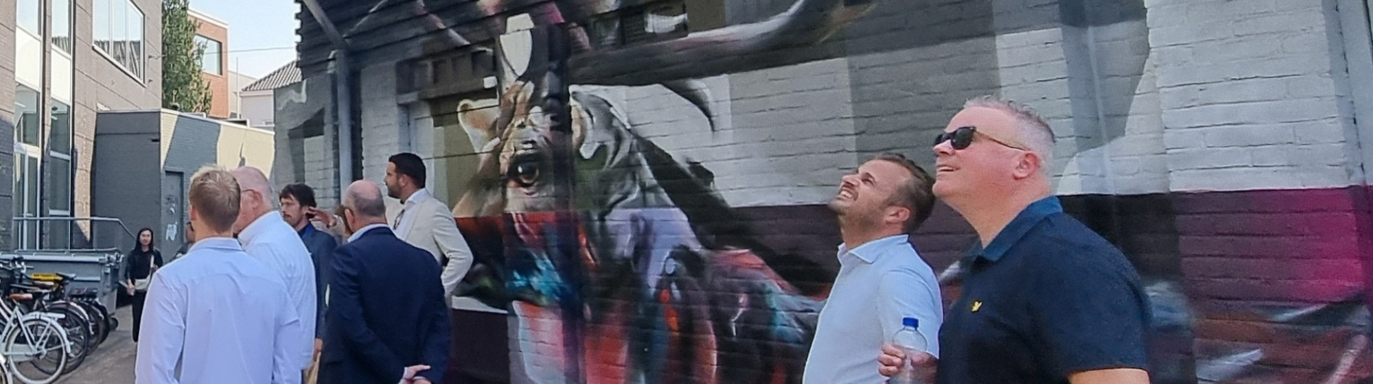 Groep bestuurders bekijkt een grote muurschildering van een hert op de gevel van een gebouw.