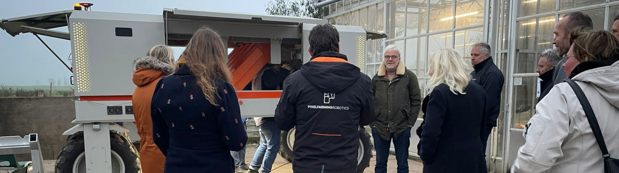Groepje deelnemers aan de Safaritour staat buiten een kas bij een landbouwrobot