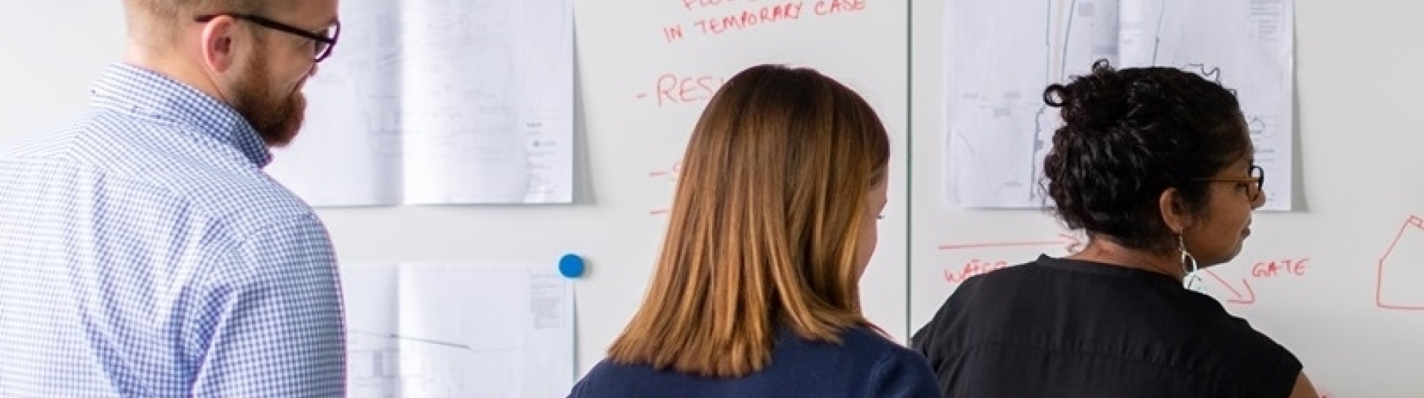 Drie mensen schrijven ideeën op op papieren aan de wand
