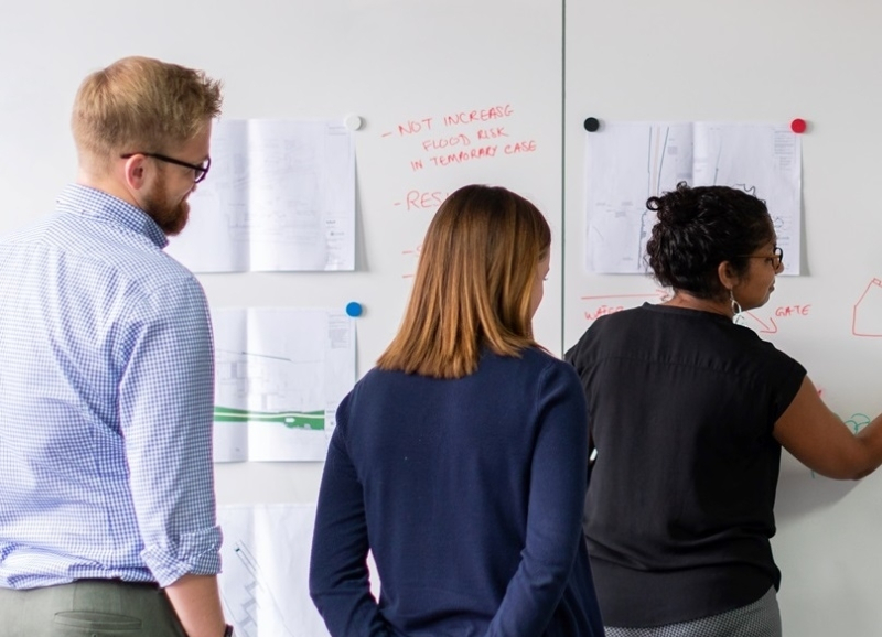Drie mensen schrijven ideeën op op papieren aan de wand