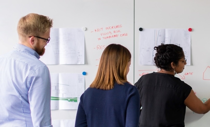 Drie mensen schrijven ideeën op op papieren aan de wand