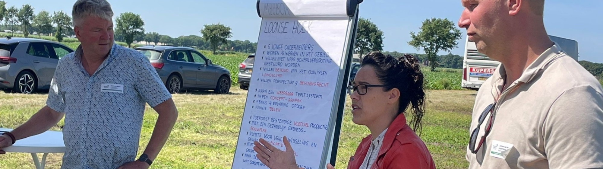 Drie deelnemers aan werkbezoek aan de AgroProeftuin op de proeflocatie met elkaar in gesprek bij een flipover 