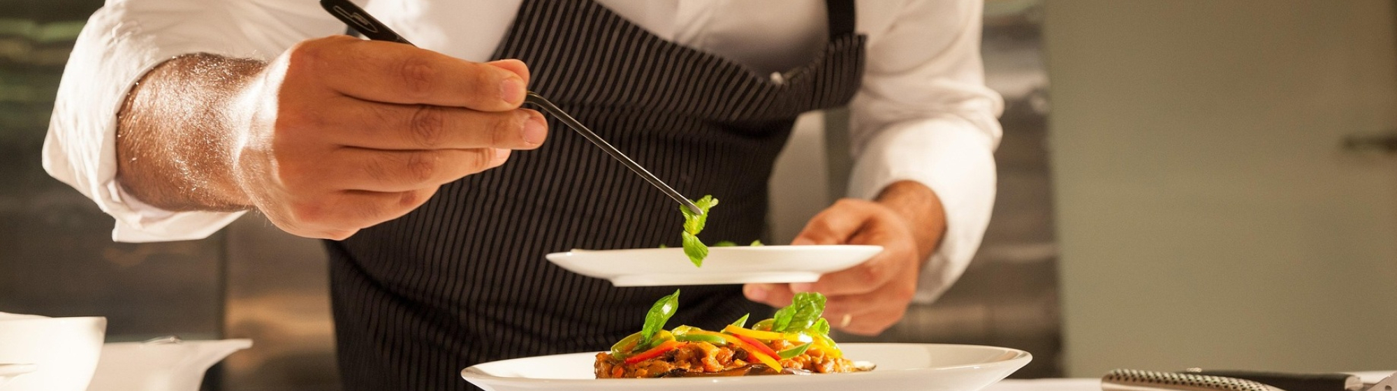 Chef-kok met schort garneert een gerecht op een bord in een professionele keuken