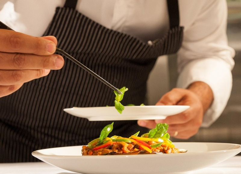 Chef-kok met schort garneert een gerecht op een bord in een professionele keuken