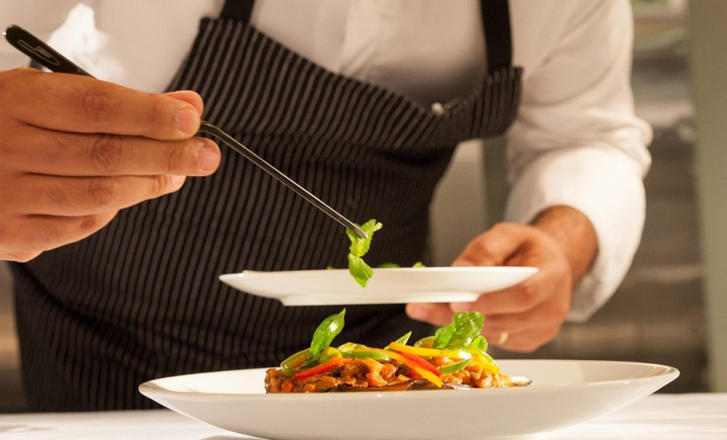 Chef-kok met schort garneert een gerecht op een bord in een professionele keuken