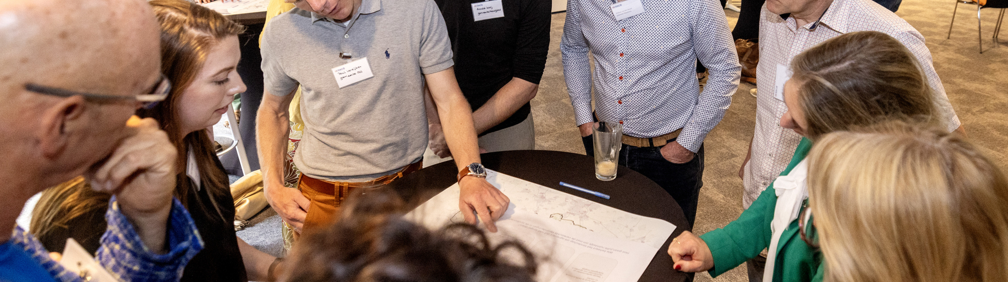Groep mensen met elkaar in gesprek rond een tafel met een grote stuk papier om op te schrijven