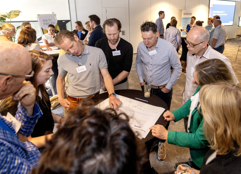 Groep mensen met elkaar in gesprek rond een tafel met een grote stuk papier om op te schrijven