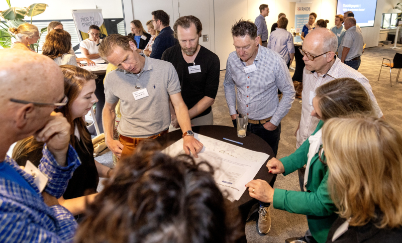 Groep mensen met elkaar in gesprek rond een tafel met een grote stuk papier om op te schrijven