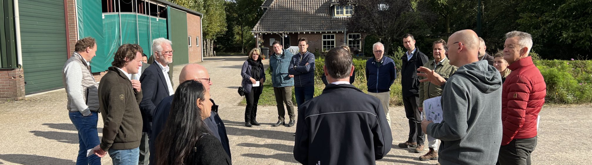 Groep mensen staat in een kring bij elkaar op een versteerd stuk grond buiten bij een boerderij op een zonnige dag
