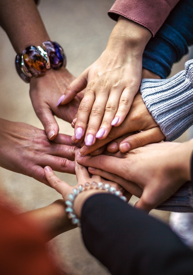 Zeven handen op elkaar die samen samenwerking uitbeelden