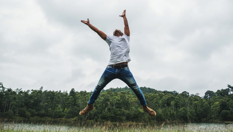 Man springt in de lucht met een meer en bomen op de achtergrond