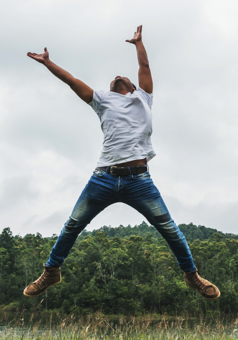 Man springt in de lucht met een meer en bomen op de achtergrond