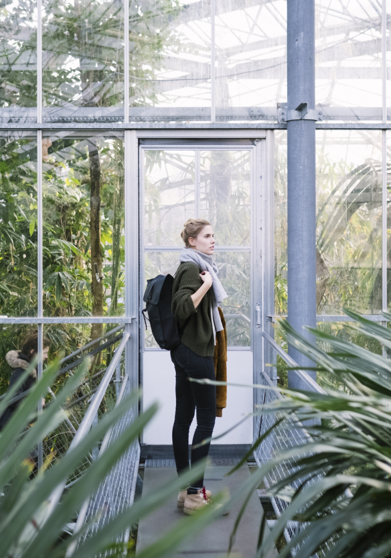 Vrouwelijke student met een rugzak in een kas met exotische planten