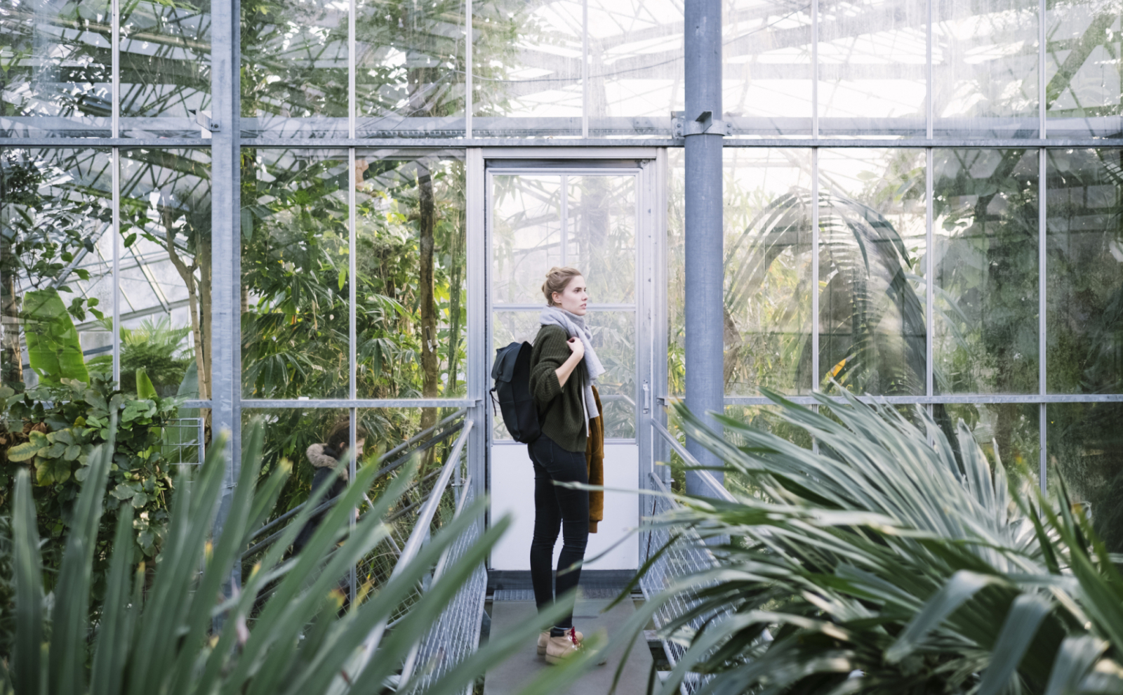 Vrouwelijke student met een rugzak in een kas met exotische planten
