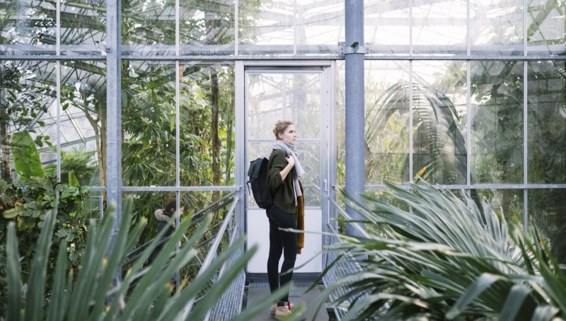 Vrouwelijke student met een rugzak in een kas met exotische planten