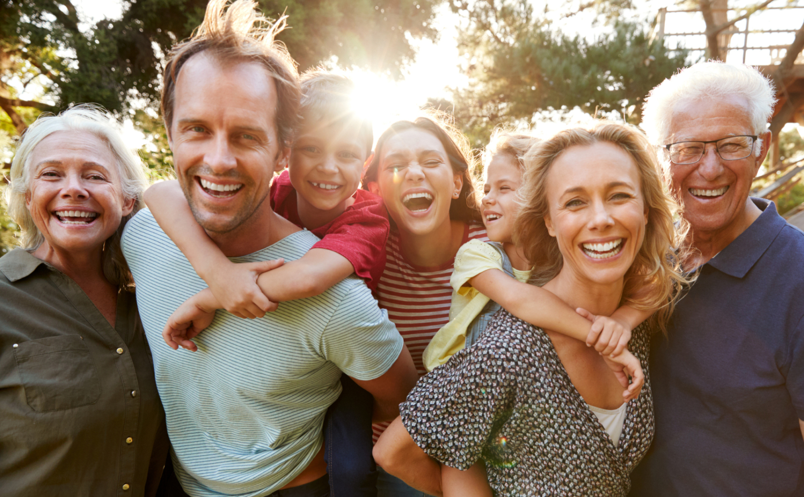 Familie met lachende opa, oma, kinderen en kleinkinderen met de zon en bomen op  achtergrond