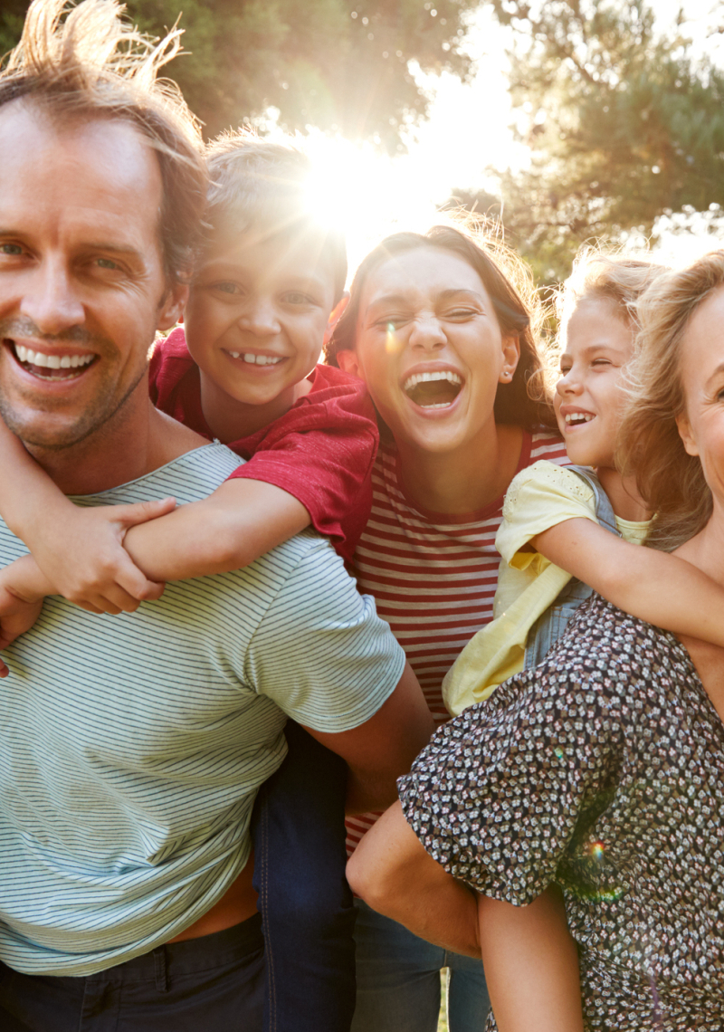 Familie met lachende opa, oma, kinderen en kleinkinderen met de zon en bomen op  achtergrond