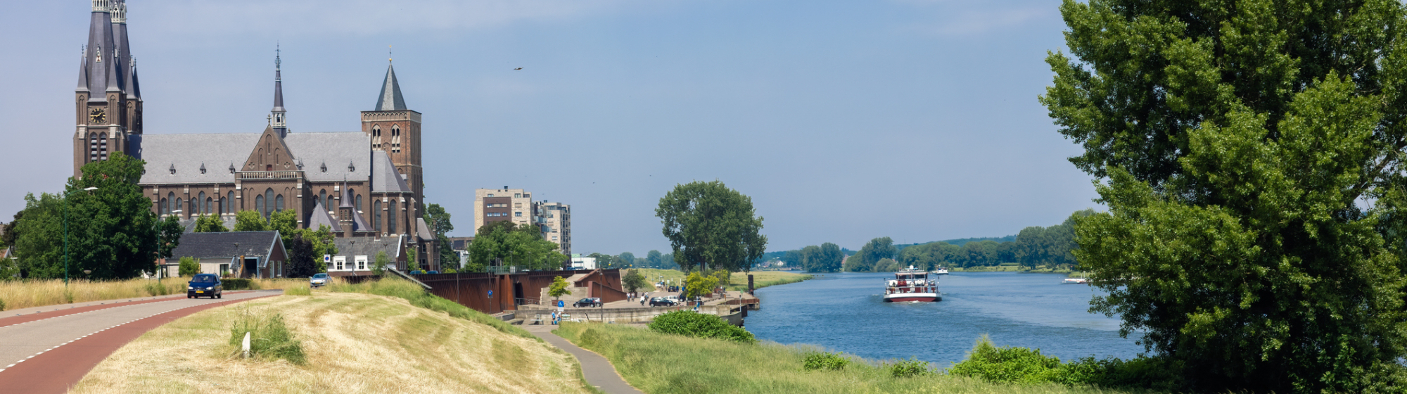 Landschap op een zonnige dag met kasteel op de achtergrond, fietspad en rivier met plezierboot