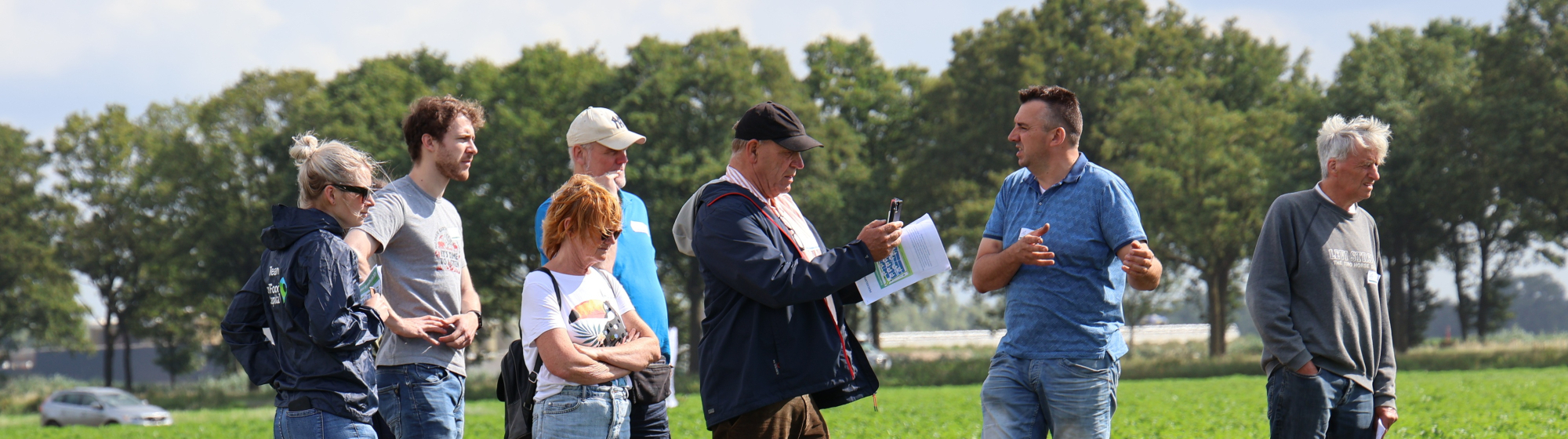 Groep agrarische ondernemers in gesprek met elkaar in een groen landbouwveld, met bomen op de achtergrond en een deels bewolkte lucht