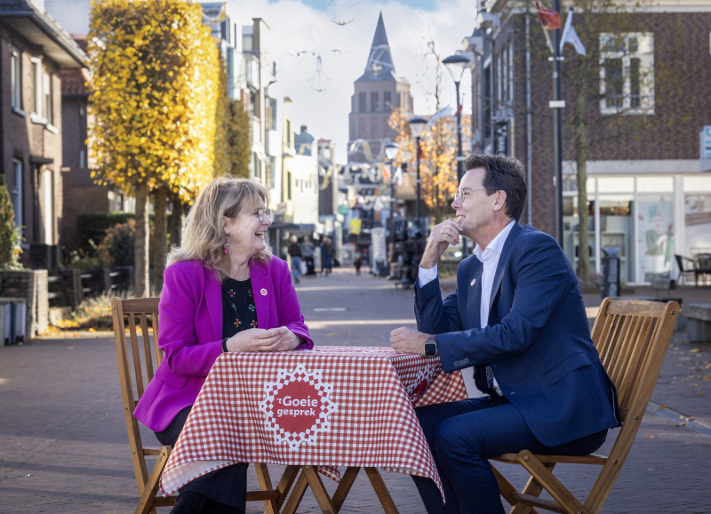 Marieke Moorman en René Peerenboom zitten aan een klein bistrostafeltje met een Brabants kleedje midden in een winkelstraat 