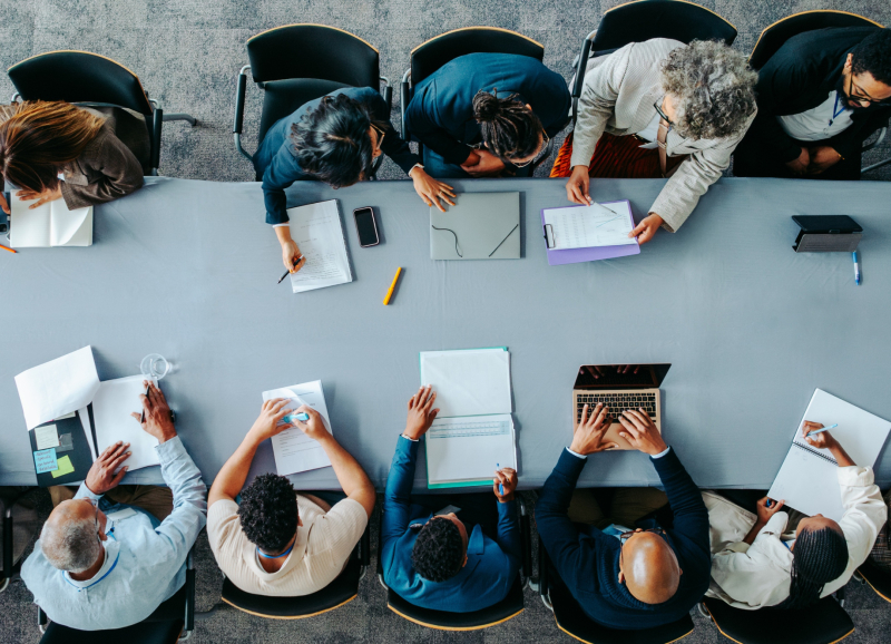 Zakelijk overleg met mensen die samenwerken aan een tafel, met notitieblokken, laptops en documenten.
