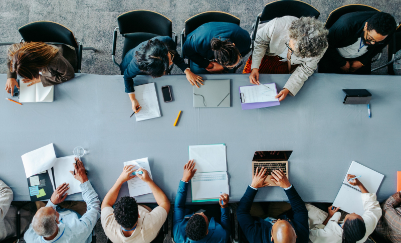 Zakelijk overleg met mensen die samenwerken aan een tafel, met notitieblokken, laptops en documenten.