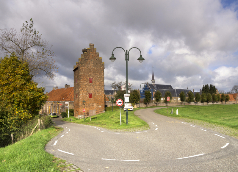 Historische toren en kerk in groen met een weg ervoor in een Noordoost-Brabants dorp met bewolkte lucht