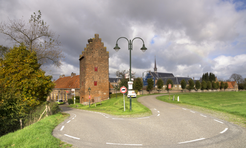 Historische toren en kerk in groen met een weg ervoor in een Noordoost-Brabants dorp met bewolkte lucht