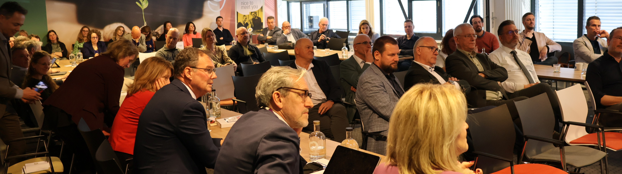 Wethouders en andere bestuurders op de bestuurlijke Regiodag in een vergaderzaal tijdens een presentatie