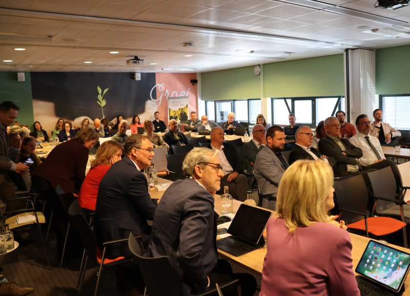 Wethouders en andere bestuurders op de bestuurlijke Regiodag in een vergaderzaal tijdens een presentatie