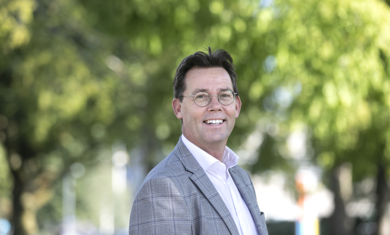 Portretfoto René Peerenboom, buiten met groene bomen op de achtergrond