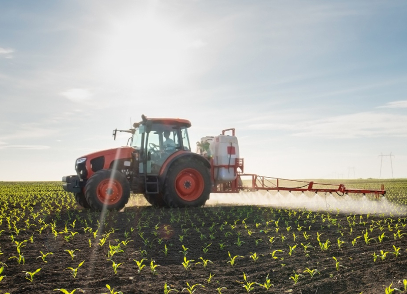 Tractor die gewasbeschermingsmiddelen sproeit op een landbouwveld tijdens zonsopkomst