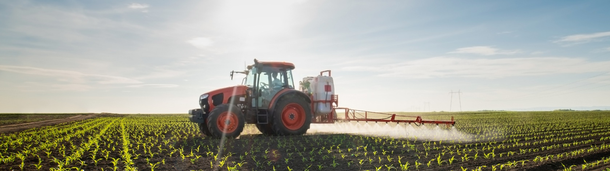 Tractor die gewasbeschermingsmiddelen sproeit op een landbouwveld tijdens zonsopkomst