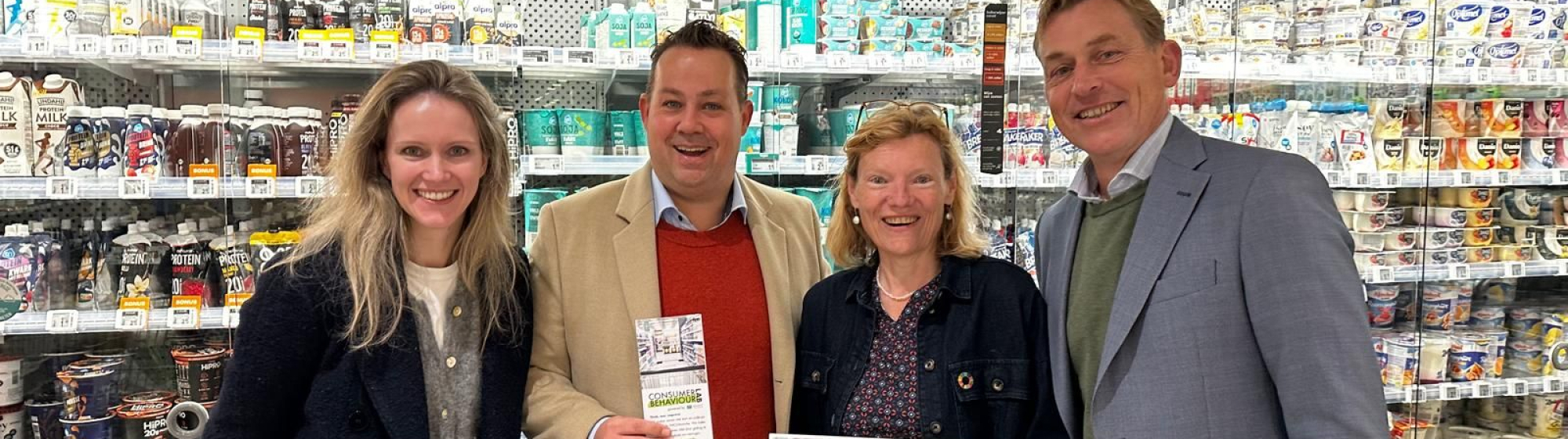 Vier betrokkenen van het CBL houden de samenwerkingsovereenkomst vast in een supermarktomgeving 